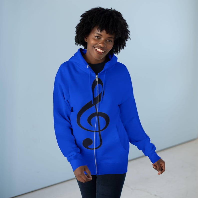 A woman wearing a royal blue zip-up hoodie printed with a black treble clef design.