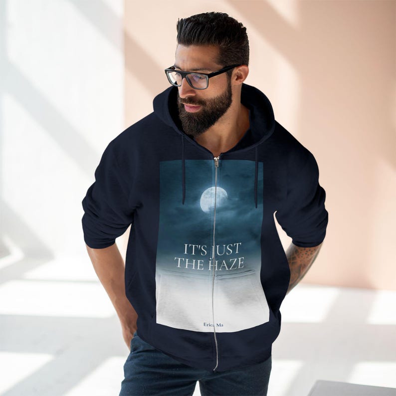 Navy blue zip-up hoodie with a full moon graphic and the text "IT'S JUST THE HAZE". The graphic features a full moon in a dark blue sky. The hoodie has a hood and a full-length zipper.