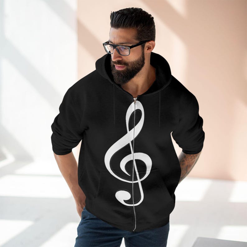 A bearded man wearing glasses and a black zip-up hoodie with a large white treble clef on the front.