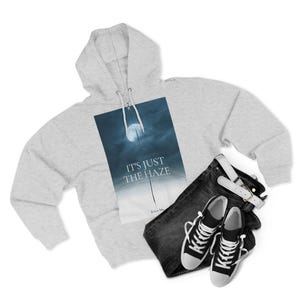 A light grey hooded sweatshirt featuring the text "IT'S JUST THE HAZE" over a moonlit image. The outfit includes black jeans, a white belt, and black and white trainers.