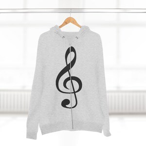 A grey zip-up hoodie with a black treble clef hanging from a wooden hanger against a neutral background.