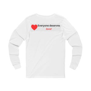 Back view of a white long-sleeve t-shirt with a rectangular graphic near the back collar displaying a red heart and the text Everyone deserves love!.