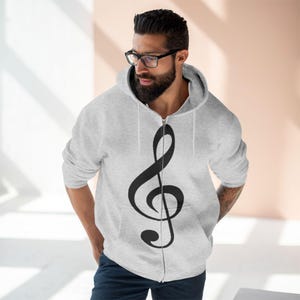 A man wearing a grey zip-up hoodie featuring a black treble clef design on the front.