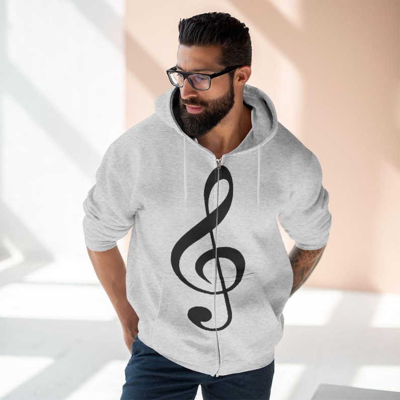 A man wearing a grey zip-up hoodie featuring a black treble clef design on the front.