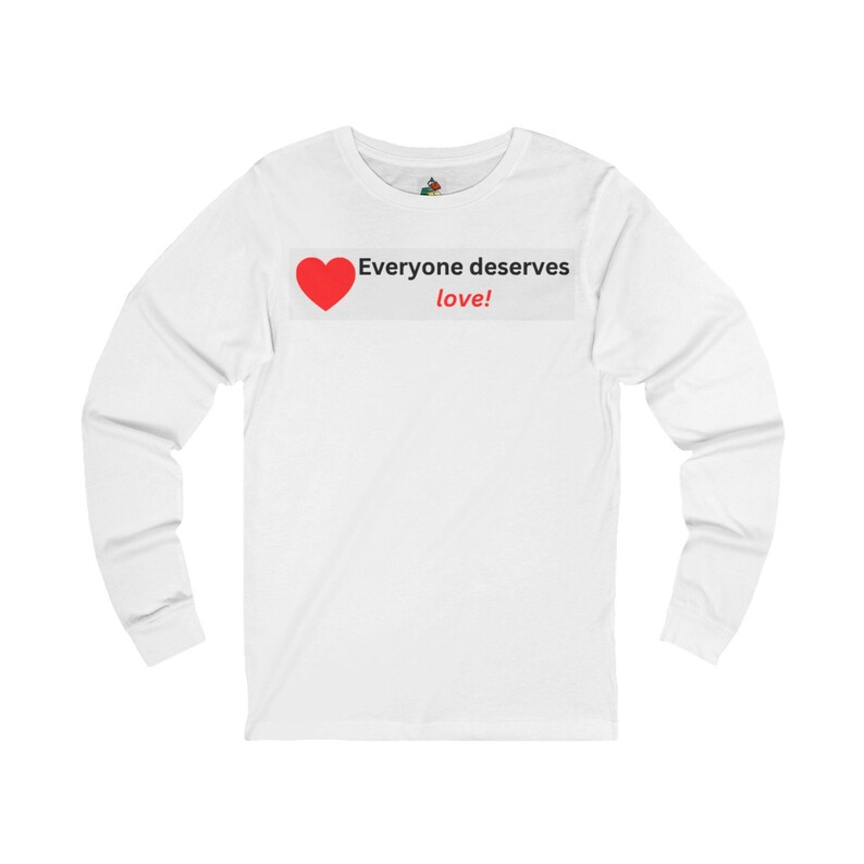 Front view of a white long-sleeve t-shirt featuring a white rectangular chest graphic with a red heart and the text Everyone deserves love!.