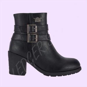 May include: A black ankle boot with a block heel and a lugged sole. The boot features two horizontal straps across the ankle, each secured with a metallic buckle. A metallic emblem depicting a winged skull is positioned on the upper outer side.