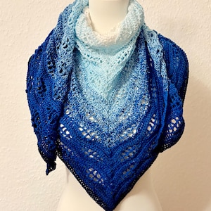 Może przedstawiać: Ręcznie robiona chusta w odcieniach niebieskiego, od jasnego do głębokiego indygo. Trójkątna chusta jest prezentowana na manekinie, prezentując skomplikowany ażurowy wzór. Efekt gradientu tworzy atrakcyjny wizualnie dodatek.