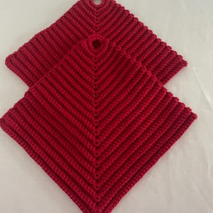 Può includere: Due presine quadrate rosse all'uncinetto. Ogni presina ha un anello per appenderla e un design a coste strutturato. Le presine sono realizzate con un filato spesso e sono di un rosso vibrante.