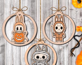 May include: Three wooden Halloween ornaments featuring bunny characters in costumes. One is dressed as a pumpkin, another as a slasher, and the third as a mummy. Each ornament is suspended by twine and has a circular frame.