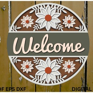 Könnte beinhalten: Runder Holzschild mit dem Wort "Welcome" in Schreibschrift. Das Schild hat ein Blumendesign mit weißen und roten Akzenten. Der Hintergrund ist eine verwitterte Holzstruktur.
