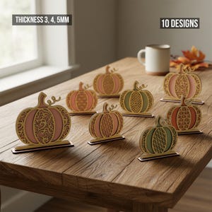 May include: Wooden pumpkin decorations in various colors, including pink, green, and orange, with intricate cutout designs. The pumpkins are displayed on a wooden table. The text in the image says "THICKNESS 3, 4, 5MM" and "10 DESIGNS".