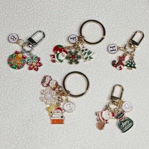 Peut inclure: Plusieurs porte-clés sur le thème de Noël. Chaque porte-clé est orné d'un anneau doré et de breloques festives, dont le Père Noël, des sapins, des flocons de neige et des sacs cadeaux. Les breloques sont rouges, vertes, blanches et dorées.