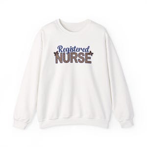 Op de afbeelding: Witte crewneck sweatshirt met de tekst "Registered Nurse" in blauw en luipaardprint. Een casual kledingstuk, ideaal voor dagelijks gebruik. Het ontwerp is centraal op de voorkant geplaatst.