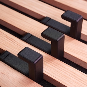 Könnte beinhalten: Nahaufnahme eines Holzbetts mit schwarzen Metallstützen. Der Rahmen hat hellfarbene Holzlatten mit dunkelbraunen Akzenten und schwarzen, L-förmigen Metallhaken zur Unterstützung. Das Design ist modern und minimalistisch.