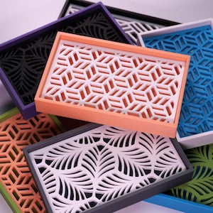 Peut inclure: Plusieurs plateaux décoratifs colorés avec des motifs ajourés géométriques et en forme de feuilles. Les plateaux sont de différentes couleurs, notamment orange, bleu, vert, violet et gris, avec des motifs intérieurs blancs ou noirs. Idéal pour la décoration intérieure.