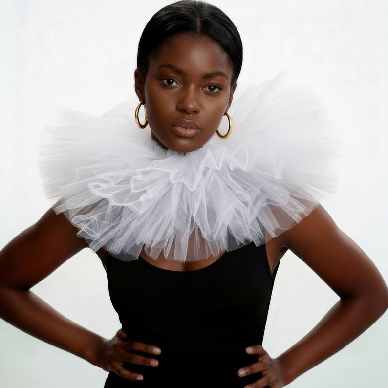 May include: A woman wearing a large, white, ruffled tulle collar over a black top. The collar is the focal point, creating a dramatic effect. Gold hoop earrings add a touch of elegance.