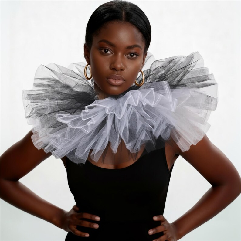 May include: A woman wearing a black tank top and gold hoop earrings, with a large, ruffled collar made of black and white tulle. The collar is layered and creates a dramatic, textured effect around the neck.