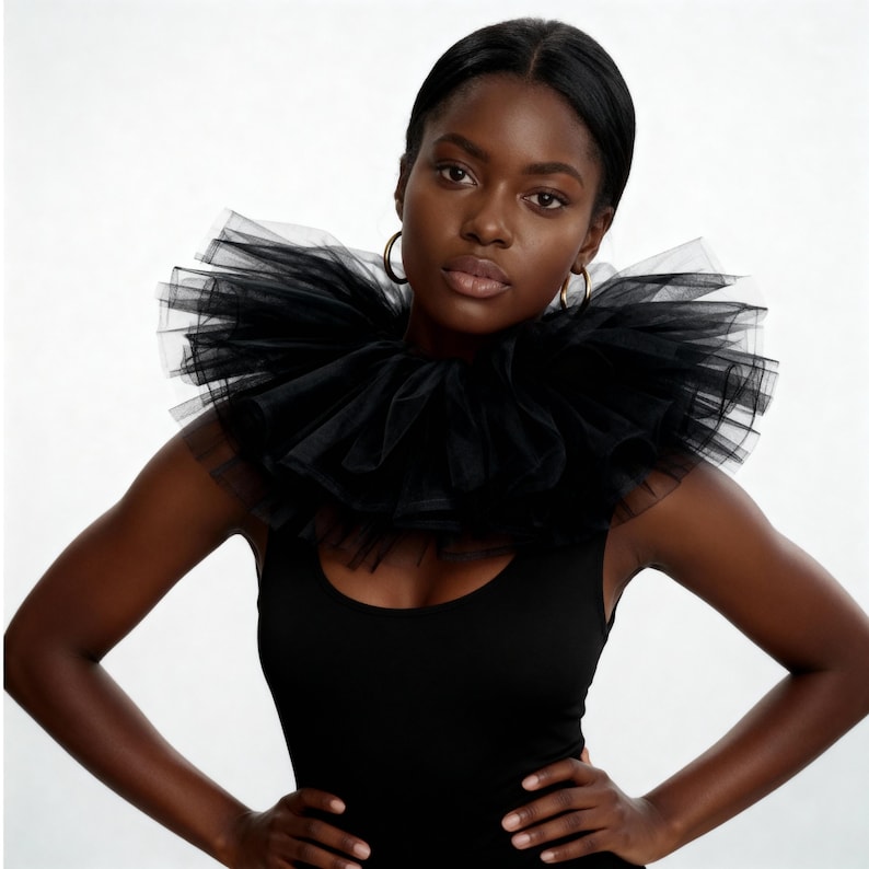 May include: A black tulle collar with multiple layers, creating a voluminous effect. The collar is worn over a black tank top. The model is wearing gold hoop earrings.