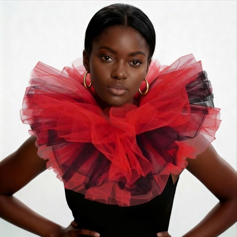 May include: A woman wearing a dramatic red and black tulle collar. The collar is layered and ruffled, creating a voluminous effect. She is also wearing gold hoop earrings and a black top.