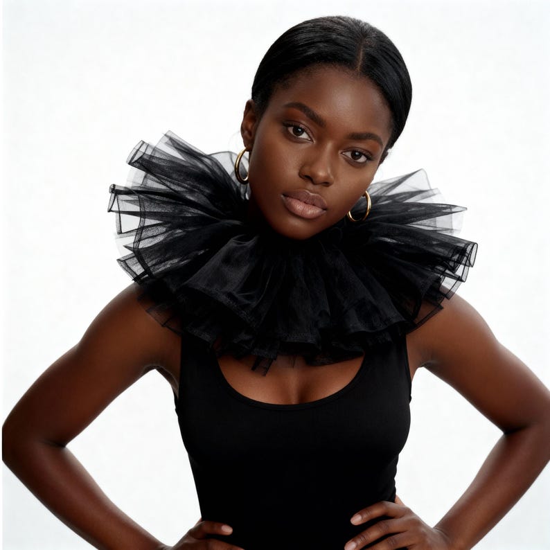 May include: A woman wearing a black tank top and a large, ruffled black collar. The collar is made of layers of sheer fabric. Gold hoop earrings are visible. The background is plain white.