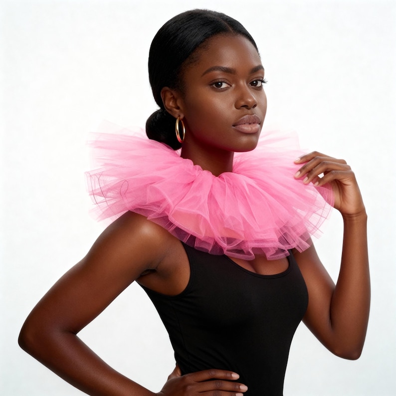 May include: A woman wearing a bright pink tulle collar over a black tank top. The collar is layered and voluminous, creating a dramatic effect. The woman has dark hair pulled back and is wearing gold hoop earrings.
