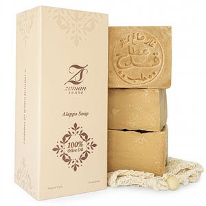 Op de afbeelding: Een stapel van vier beige Aleppo-zepen met Arabische schriftstempels, naast een beige Zaman Sense-doos. De doos toont de tekst "Aleppo Soap" en "100% Olive Oil". De zepen liggen op een witte doek.