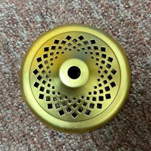 May include: A gold-colored metal incense burner lid with a central hole and a decorative diamond-shaped pattern. The lid is circular and has a raised center.