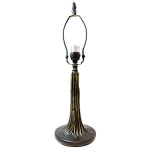 May include: A table lamp base with a dark bronze finish and gold-toned highlights, featuring a textured, tree-trunk-inspired stem. The lamp includes a black socket, a metal harp, and a decorative finial at the top, standing on a circular base.