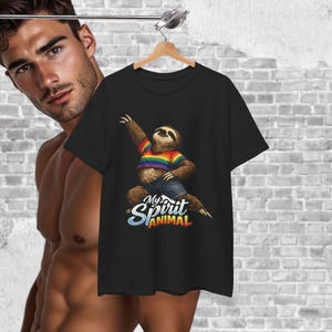 Puede incluir: Camiseta negra con un perezoso de dibujos animados que lleva una camiseta a rayas arcoíris y vaqueros azules. El perezoso está en una pose de baile con el texto "My Spirit Animal" en una fuente colorida.