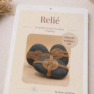 May include: A digital tablet displays a guide on stone wrapping, with the title "Relié" and the text "Un guide complet du stone wrapping." The image features three dark stones wrapped with woven twine, labeled "Nouvelle tendance DIY."