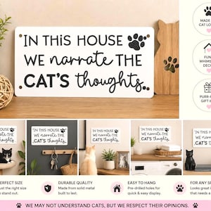 May include: A white metal sign with the text "IN THIS HOUSE WE narrate THE CAT'S thoughts." in black. The sign has a paw print graphic and is displayed with other cat-themed decor. The sign is a purr-fect gift idea.