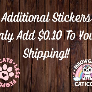 May include: Two circular stickers on a dark wood background. The left sticker is pink with a paw print and the text MORE CATS LESS PEOPLE. The right sticker features a white cat with a unicorn horn, a rainbow, and the text MEOWGICAL CATICORN.