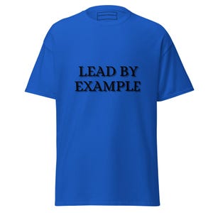 May include: A royal blue t-shirt with the phrase "LEAD BY EXAMPLE" printed in black, bold letters across the front. The shirt has short sleeves and a crew neck.