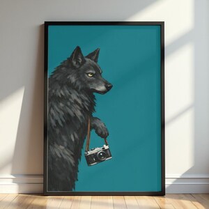 May include: Framed art print featuring a black wolf with yellow eyes holding a vintage camera. The wolf is set against a teal background. The artwork is in a black frame and is displayed against a white wall.