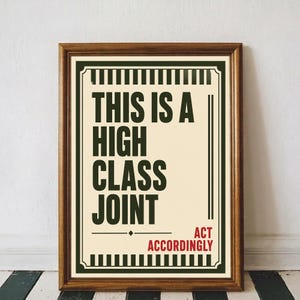 Peut inclure: Une affiche encadrée sur fond crème avec le texte vert foncé THIS IS A HIGH CLASS JOINT et le texte rouge ACT ACCORDINGLY. Le design présente des bordures à rayures vert foncé et une fine ligne horizontale décorative au centre.
