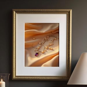 Puede incluir: Una imagen enmarcada de un collar de oro con perlas y una gema púrpura sobre una tela dorada. La imagen está en un marco dorado y se muestra sobre una superficie de mármol blanco. Una lámpara blanca y velas en candelabros negros también están presentes.