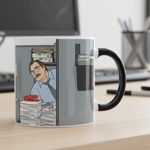 May include: White ceramic mug with a cartoon illustration of a man peeking from a gray office cabinet. The mug has a black handle and a stack of papers with a red stapler.