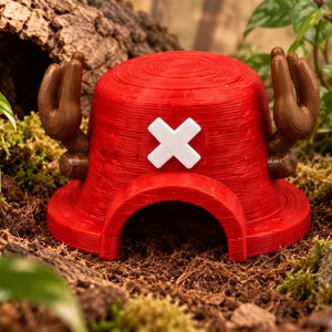 May include: A bright red, dome-shaped structure featuring a prominent white cross symbol on the front and two brown, antler-like protrusions extending from the sides. The object has a hollow arched opening at the base and a textured surface.