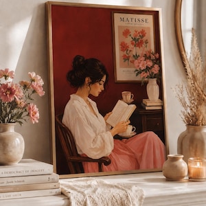 Peut inclure: Une impression d'art encadrée représentant une personne aux cheveux bruns en chignon, vêtue d'une chemise blanche à manches longues et d'une jupe rose, assise sur une chaise en bois en train de lire. L'image inclut une affiche Matisse et des tasses.