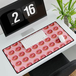 Peut inclure: Tapis de souris rectangulaire rose avec un motif de beignets glacés. Les beignets ont un glaçage rose et sont disposés en motif répétitif. Un clavier et une souris blancs sont posés sur le tapis, à côté d'un écran d'ordinateur.