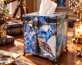 Puede incluir: Una caja cuadrada de madera para pañuelos con un diseño de mapa celestial en tonos azul oscuro y morado, una ilustración de un búho y un cierre de metal. La caja se eleva sobre cuatro patas metálicas ornamentadas e incluye una borla marrón.