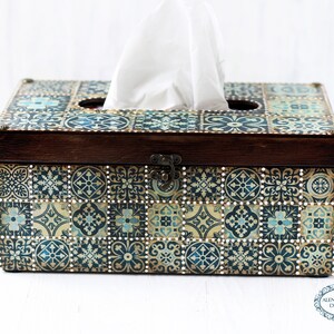 May include: A wooden tissue box cover with a decorative design of blue, gold, and white tiles. The box has a hinged lid and a cutout for tissues.