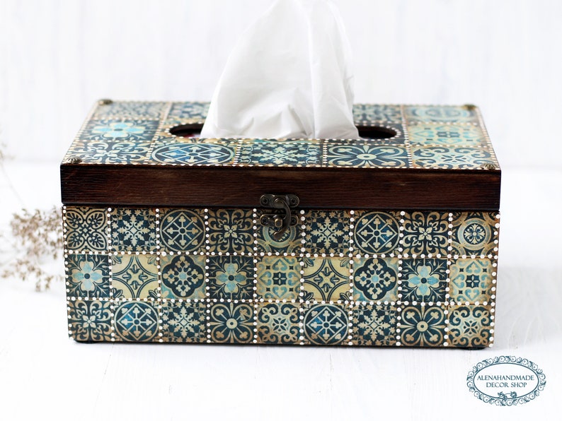 May include: A wooden tissue box cover with a decorative design of blue, gold, and white tiles. The box has a hinged lid and a cutout for tissues.