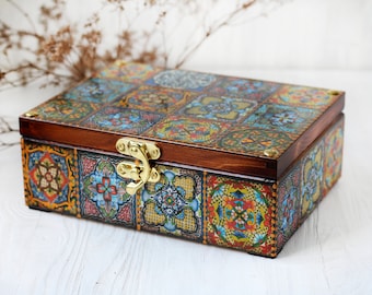 May include: A rectangular wooden box featuring a vibrant, multi-colored tile pattern on the lid and sides. The box has a dark wood finish and is secured with a polished gold-tone metal latch on the front. The surface displays intricate floral and geometric motifs in shades of blue, red, yellow, and green.