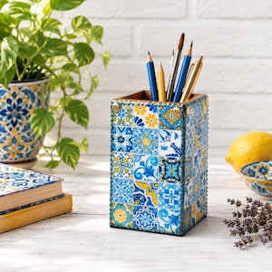 May include: A rectangular pencil holder featuring a vibrant blue and yellow tile pattern with intricate floral and geometric motifs. The container is filled with various colored pencils and pens, and it is accented with small gold-toned metal studs.