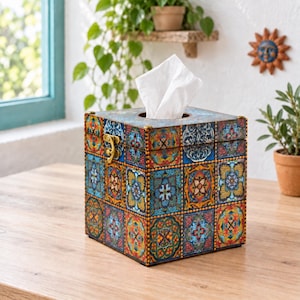 May include: A square tissue box cover featuring a vibrant, multi-colored tile pattern in shades of blue, orange, yellow, and red. The box has a hinged lid with a gold-toned metal latch on the front and a circular opening at the top for tissues.