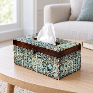 Puede incluir: Una caja rectangular para pañuelos con un marco de madera marrón oscuro y una tapa decorada con un patrón repetitivo de azulejos geométricos en tonos azules, turquesas y crema. Un pañuelo blanco asoma por la abertura.
