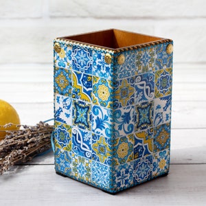 May include: A blue and yellow ceramic utensil holder with a decorative tile pattern. The holder is made of wood and has a rectangular shape.