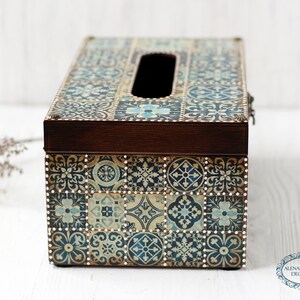 May include: A wooden tissue box cover with a decorative design of blue and white tiles. The box has a slot for tissues and a brown wooden lid.