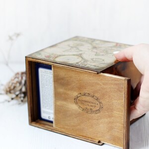 May include: A square wooden box with a sliding lid featuring a vintage map print on top. The front panel of the box is made of dark stained wood and displays the text ALENAHANDMADE DECOR SHOP inside an oval decorative border frame.